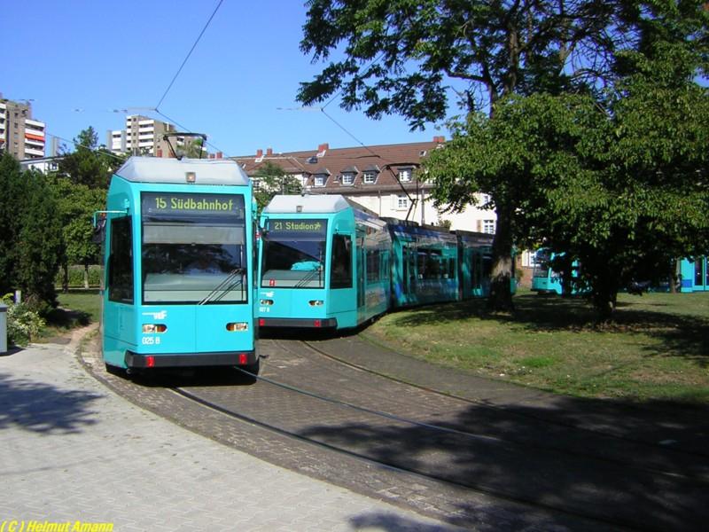 Hochbetrieb am Haardtwaldplatz am 28.08.2005: Ein Falschparker in der Rennbahnstrae sorgte dafr, da die Linie 21 kurzfristig ber den Haardtwaldplatz umgeleitet werden mute, so da dort kurzzeitig beide Gleise befahren wurden. Der Zufall wollte es, da auch noch zwei Triebwagen vom Typ R nebeneinander standen. Links die dort planmig endende Linie 15 mit Triebwagen 025 und rechts der 7. Zug der Linie 21 mit dem Triebwagen 027, beide aus der 
zweiten Bauserie dieses Wagentyps. Der dritte R-Triebwagen im
Bunde wartete bereits im Hintergrund. 