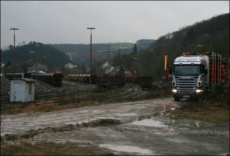 Holzverladeplatz am Abend: Whrend in der linken Abstellgruppe leere Schotterwaggons abegstellt stehen an der Ladestrae die Holztansportwaggons zur Abholung bereit. Rechts im Bild bringt ein SCANIA R470 mit 470 PS die nchste Ladung Fichtenholz. (06.02.2007)