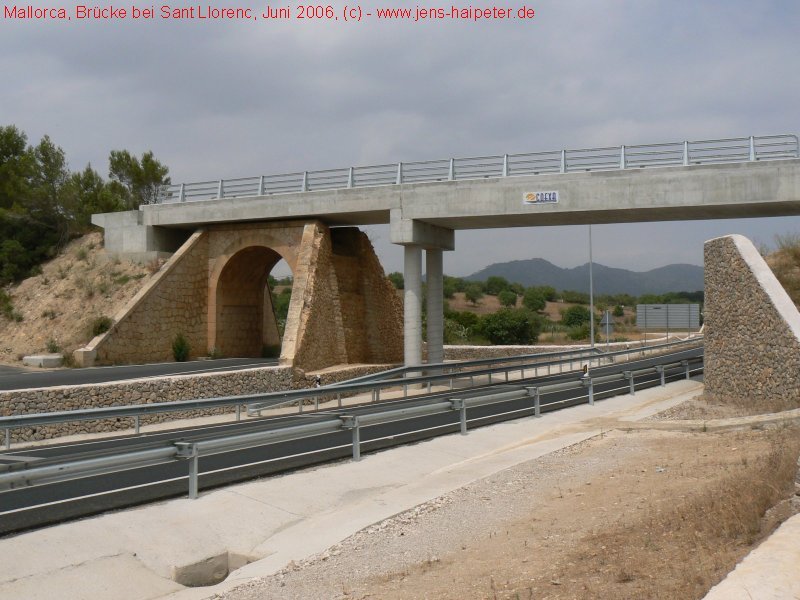 Im Zuge des Neubaus der Umgehungsstrae von Sant Llorenc de Cardasar (C-715) wurden zwei Brcken neu errichtet. Die hier abgebildete befindet sich ca. 0,5 km vom Bahnhof entfernt in Richtung Art. Der Bau ist 2002/2003 erfolgt. Interessanter Weise wurde die alte Steinbogenbrcke gelassen, wo sie ist und eine vollkommen neue Betonbrcke darber gebaut. Allerdings sind an dieser Stelle noch keine Gleise in Sicht. Siehe auch Darstellung von der anderen Seite aus. Foto: Juni 2006
