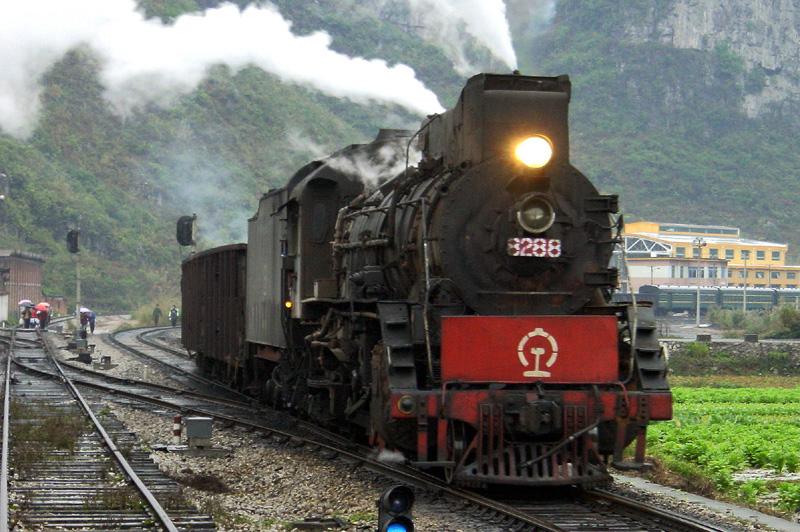 JS 8288 berfhrt hier mit dem planmigen Personenzug einig Gterwagen Richtung Hechi - im Hintergrund die noch im Bau befindliche neue Wartungshalle fr Dieselloks, Dezember 2002 