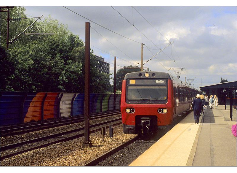 Kopenhagen, eine S-Bahn-Stadt -

Die S-Bahn Kopenhagen hat eine Streckenlänge von ca. 170 km mit 85 Bahnhöfen. Sie fährt unabhängig vom anderen Eisenbahnverkehr auf eigenen Gleisen unter einer 1500 V Gleichstrom-Oberleitung. Die Stammstrecke in der Innenstadt verläuft parallel zur Fernbahn, darin eingeschlossen ist ein 1,5 km langer Tunnel mit der unterirdischen Station  Nørreport . Aufnahme 1990 im Bahnhof  Brøndbyøster   mit einem Triebwagen der 3.Generation, von denen es nur 8 Vierwagenzüge gibt. 

Sommer 1990, Scan vom Dia (M)