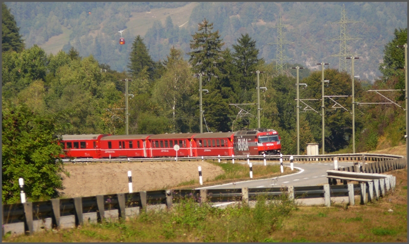 Lngs der Kantonsstrasse zwischen Rhzns und Rothenbrunnen erscheint der RE1141 mit Ge 4/4 III 646 auf der Fahrt von Chur nach St.Moritz. Zur gleichen Zeit berquert die Luftseilbahn Rhzns - Feldis die Rheinschlucht. Eine der beiden runden Kabinen ist links ber dem letzten Fahrleitungsmasten zu erkennen. (01.10.2009)