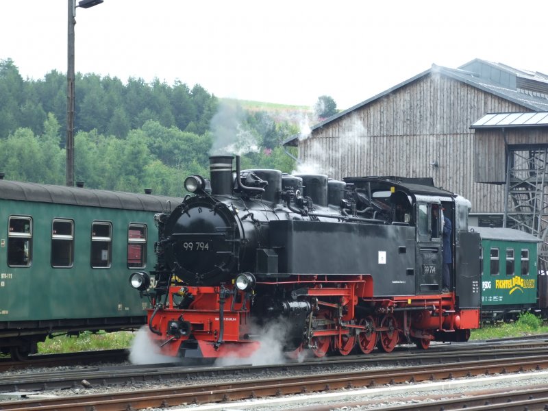 Lok 99-794 der Fichtelbergbahn hat nach Kohle bunkern und Wasser fassen sich auf den Weg gemacht, den Wagenpark auf der anderen Seite des Bahnhofes anzukuppeln. Im Hintergrund stehen ein paar abgestellte Wagen und ebenso zu sehen ist ein Teil des Lokschuppens.
Oberwiesenthal, der 23.7.08