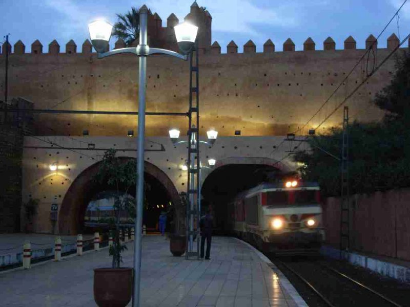 Lok E-1354 fhrt mit dem frhen Schnellzug nach Fes (ab 07:17) im Bahnhof Rabat-Ville, welcher in einem Einschnitt zwischen zwei Tunnels liegt, ein.
Die Unterbaureihe E-1350 wurde in 9 Exemplaren 1999 in Dienst gestellt. Diese Unterbaureihe ist mit einer Leistung von 4500kW derzeit die leistungsfhigste in Marokko. Mit einer Hchstgeschwindigkeit vom 120km/h wird sie vornehmlich im Gterverkehr eingesetzt.
24.01.2007 Rabat-Ville