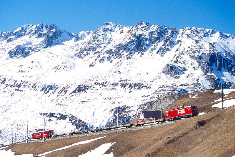 MGB FO-AUTOTRANSPORTZUG 4346 Von Andermatt nach Sedrun am 15.02.1998 bei Mettlen mit Zahnrad-E-Lok HGe 4/4II 105 - Sklv 4832 - Sklv 4834 - Rvw 4798 - Sklv 4833 - RhB B 2213. Hinweis: Lok noch in alter Lackierung.
