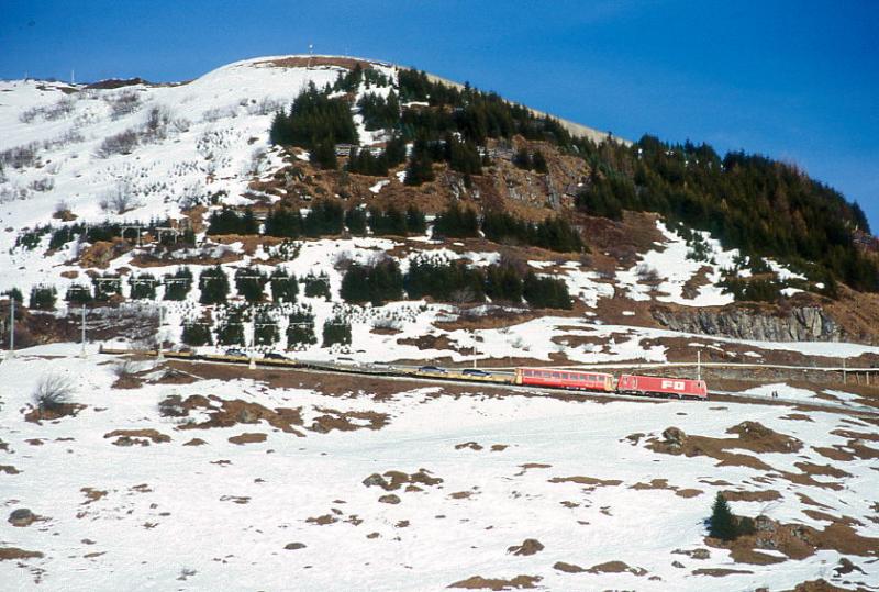 MGB FO-AUTOZUG 4353 von Sedrun nach Andermatt am 15.02.1998 zwischen Biel-Kehrtunnel und Butzen-Kehrtunnel mit Zahnrad-E-Lok HGe 4/4II 105 - RhB B 2213 - Sklv 4833 - Rvw 4798 - Sklv 4834 - Sklv 4832. Hinweis: FO-Lok noch in alter Lackierung.
