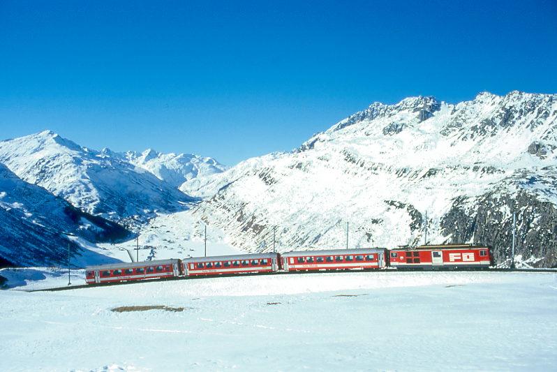 MGB FO-DIENSTZUG 6829 von Oberalppass-Calmot nach Andermatt am 15.02.1998 etwa 400m unterhalb von Ntschen mit Steuerwagen voraus ABt 4158 - B 4282 - B 4281 - Zahnrad-Gepcktriebwagen BDeh 4/4II 93. Hinweis: Fahrzeuge noch in alter Lackierung. Der abgelichtete Dienstzug ist die Rckleistung eines Wintersportzuges der die Wintersportgebiete Ntschen und Oberalppass von Andermatt aus wegen Massenandrang von Sportlern flexibel auf der einspurigen Strecke zustzlich bedient. Der Zug schlngelt sich hier bremsend in einen 4193m langen Zahnstangenabschitt mit 110 Promille Geflle in mehreren Serpentinen von Ntschen nach Andermatt im Urserental hinab. In der Mittagszeit ist im hochalpinen Urserental etwas Sonne. Blick nach Westen zum 2431m hohen Furkapass, der ber der Triebwagenspitze erkennbar ist. Allerdings ist nicht mehr der ganze Zug in Sonne abzulichten. 
