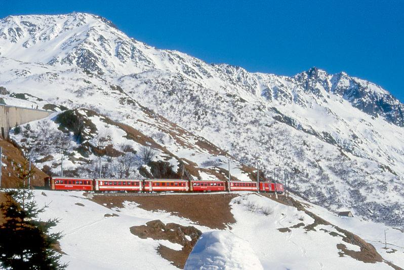 MGB FO-ENTLASTUNGSZUG 356 von Andermatt nach Disentis am 15.02.1998 oberhalb Ortseingang von Andermatt mit Zahnrad-E-Lok HGe 4/4II 104 - D 4342 - B 4263 - RhB B 2255 - ABt 4195 - B 4268 - RhB B 2212. Hinweis: FO-Fahrzeuge noch in alter Lackierung. Der Entlastungszug wurde kurzfristig in Andermatt gewendet um weitere Sportler aus den Sportgebieten Ntschen und Oberalppass am spten Nachmittag wegen groen Fahrgastaufkommen ohne lange Wartezeiten zu Tal zu bringen.
