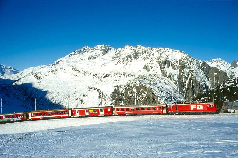 MGB FO-REGIONALZUG 324 von Andermatt nach Disentis am 15.02.1998 kurz vor Ntschen mit Zahnrad-E-Lok HGe 4/4II 101 - RhB B 2422 - DZ 4354 - B 4270 - RhB B - AB 4172 - B 4288. Hinweis: FO-Fahrzeuge noch in alter Lackierung, links unten liegt im Schatten das hochalpine Userental. Die strkste Meterspur-Zahnradlok der Welt bringt die 1863 KW Leistung in der langen 110-Promille Steigung zu 1/3 ber Adhsion und 2/3 ber Zahnrad auf die Schiene- 
