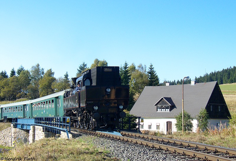 Mit bereits geschlossenem Regler rollt 354 195 am 26.09.2009 in den Bahnhof von Horny Blatna (Bergstadt Platten). Der gelbe  Fleck , welcher sich auf der Tenderrckwand spiegelt, ist das Bahnhofsgebude.