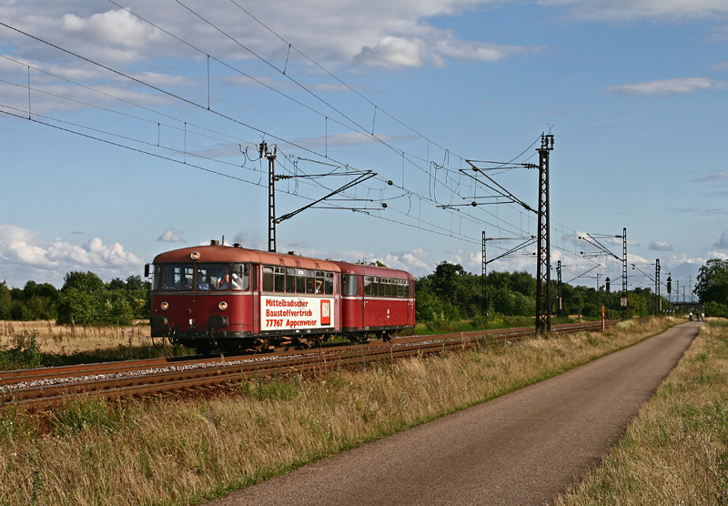 Nach erledigten Sonderfahrten zwischen Graben-Neudorf und Germersheim ist die zweiteilige Schienenbusgarnitur der Pfalzbahn, gebildet aus dem fhrenden 798 818 sowie dem Steuerwagen 998 746, am Abend des 19. Juli 2009 bei Waghusel in Richtung Schwetzingen unterwegs.