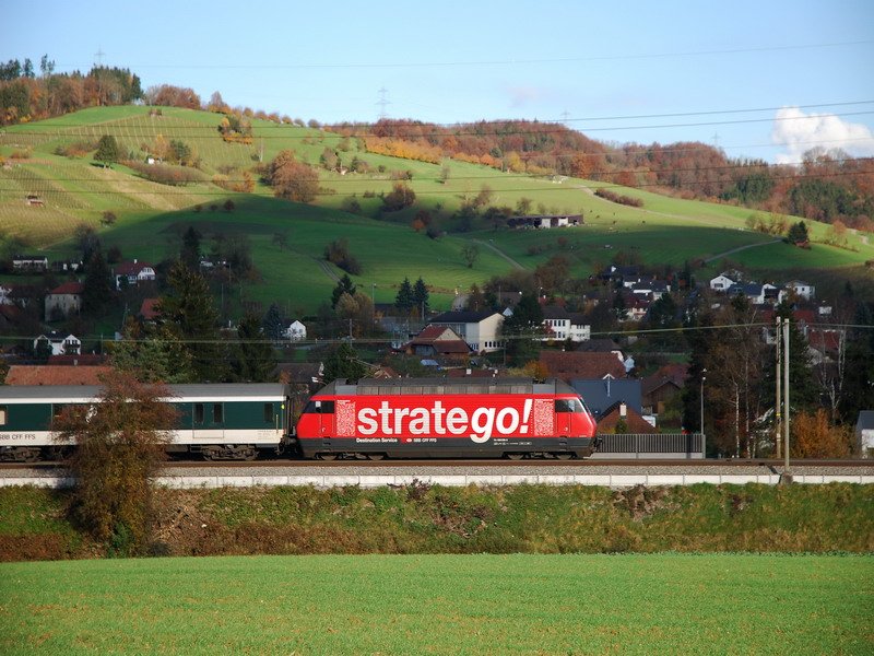 Re 460 038-3. Die rote  stratego  Werbelok, von Basel kommend, leuchtet vor dem IR 2077 im Fricktal/Aargau. Im Hintergrund ist die Ortschaft Oeschgen. 18.11.2006.