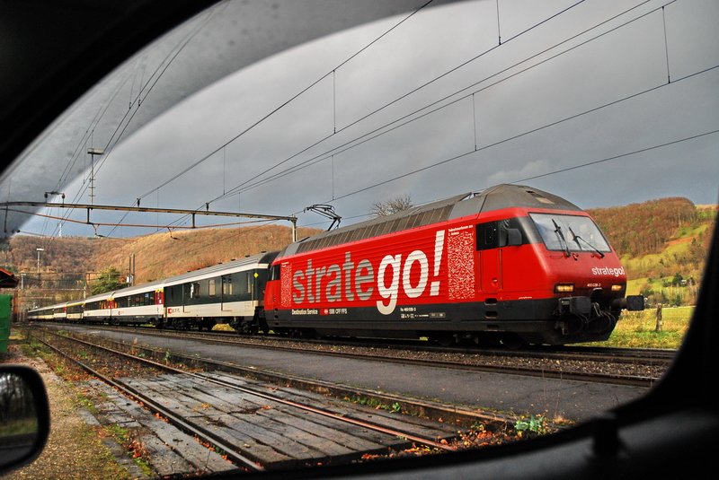 Re 460 038-3. Wie auch in Bild ID 78487 zu sehen, fotografiere ich bei Regenwetter aus dem Auto. Diesmal durch das Seitenfenster mit runtergelassener Scheibe. Der teilweise sichtbare Fensterrahmen ist beabsichtigt. Die rote  stragego  Lok macht sich gut vor dem dunklen Hintergrund. Im Fricktal (Kanton Aargau) am 4.12.2006