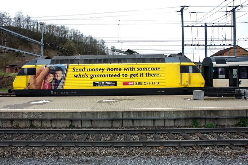 Re 460 042-5. Das leuchtende Gelb der  Western Union  Lok mit einem InterRegio ist hier im Bhf. Frick (Kanton Aargau) zu sehen. Die Werbeaufschrift in englischer Sprache verwundert, nicht jeder kann halt englisch. Dafr ist die andere Seite wenigstens in franzsischer Schrift (siehe Bild ID93699). 25.3.2007