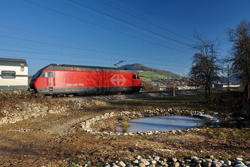 Re 460 072-2. Dieses mit einem Polfilter aufgenommene Bild zeigt eine schiebende, knallrote 460er, hinter einem InterRegio auf der Fahrt nach Basel. Im Hintergrund der Frickberg, vorn ein angelegter Teich von Naturschtzern. Durch den Polfilter wird das Blau des Himmels und das Rot der Lok besonders betont. Bei Frick (Kanton Aargau) am 30.1.2007