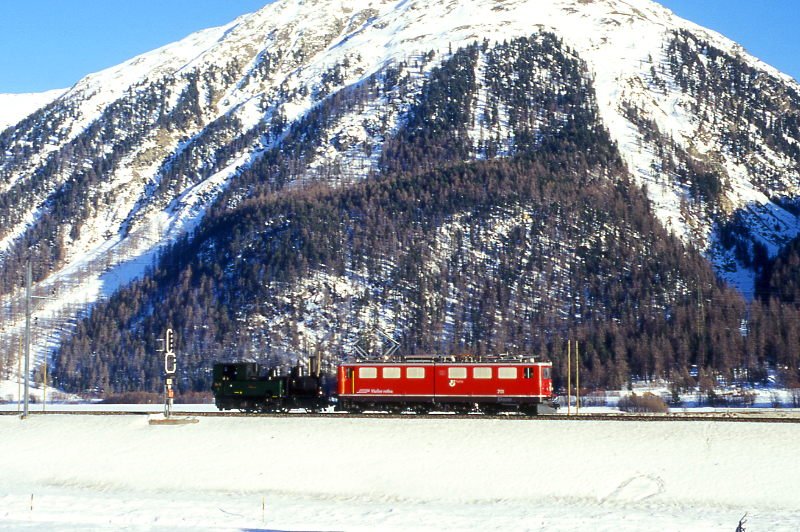 RhB Extra-Gterzug 5353 von Thusis nach Samedan fr Dampffreunde der Rhtischen Bahn am 20.02.1998 zwischen Bever und Samedan mit E-Lok Ge 6/6 II 701 (Rhtia) - Dampflok G 3/4 1 (Rhtia). Hinweis: E-Lok noch mit Scherenpantograf, Dampflok unter Dampf, gescanntes Dia
