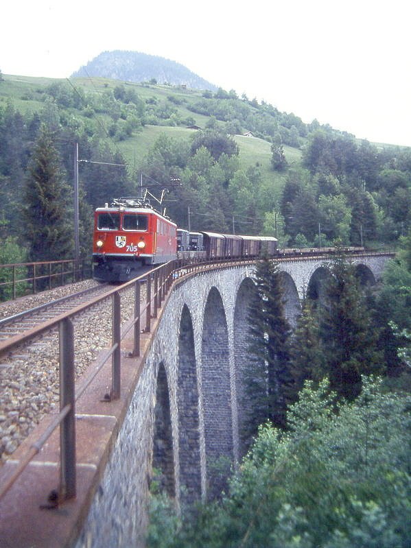RhB Gterzug 5556 von St. Moritz nach Landquart am 02.06.1992 auf Schmittentobel-Viadukt zwischen Filisur und Alvaneu mit E-Lok Ge 6/6 II 705 - Rpw - 4x Gb - 5x Kkw. Hinweis: sehr trbes Wetter, Lok noch mit Scherenpantografen, gescanntes Dia.
