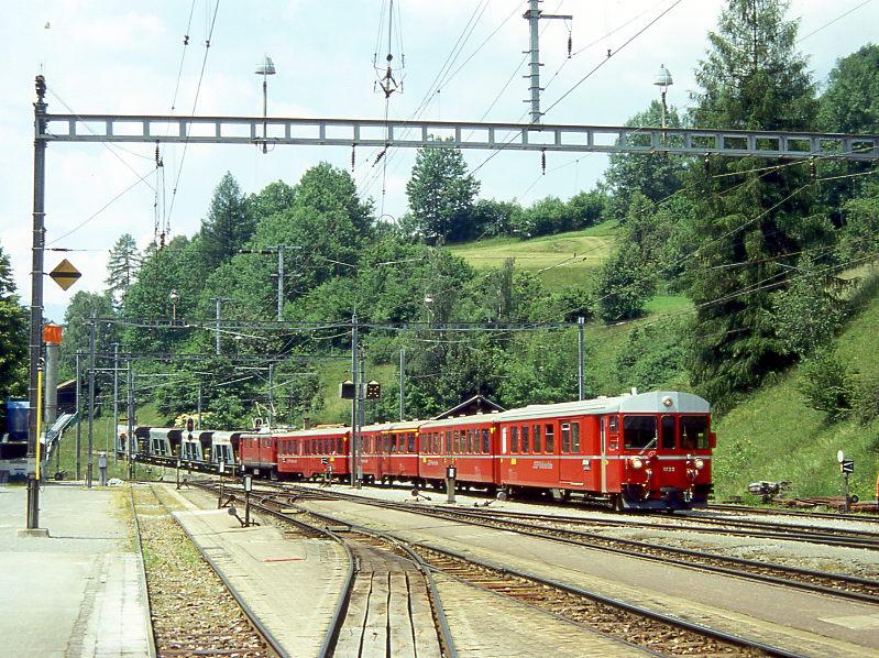 RhB Regionalzug 141 von Davos-Platz nach Filisur vom 28.06.1995 Einfahrt Filisur mit Steuerwagen vorraus BDt 1722 - B 2338 - B 2337 - AB 1515 - E-Lok Ge 4/4I 605 - Fad 8731 - Fad 8732 - Fad 8726 - Fad 8739. Hinweis: Dies ist ein NEUPENDELZUG, der aus umbebauten und modernisierten Mitteleinstiegswagen in mittelschwerer Stahlbauart der 40er-Jahre zusammengestellt wurde. Es gibt drei Kompos dieser Art. Da zwischen Davos und Filisur normalerweise keine Plangterzge verkehren, werden die hier anfallende Gterwagen den Regionalzgen angekuppelt. Hier ist die alte westliche Einfahrt von Filisur mit den Gleisen 1 bis 5 sichtbar. Links fhrt das Gleis abwrts Richtung Landwasserviadukt/Tiefencastel. Ganz links vom Gleis 1 abzweigend ist das Ladegleis/Stumpengleis zu sehen. Hier werden die gerade zugefhrten leeren Schttgutwagen ber das noch sichtbare Frderband mit Schotter beladen.