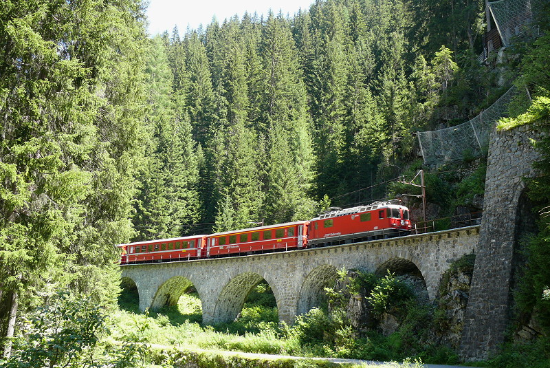 RhB - Regionalzug 1825 von Davos Platz nach Filisur am 26.07.2009 kurz nach Davos Monstein mit E-Lok Ge 4/4II 620 - A 1243 - B 2297 - B 2295 - B 2350 - BDt 1758. Hinweis: Der Zug befindet sich auf den 50,50m langen Schmelzbodenviadukt mit fnf Bogenffnungen zu 1x8, 2x12, 2x8m, Brckennmitte bei km 60,655, rechts daneben beginnt der 240,60m lange Eistbeli-Tunnel mit Portal bei km 60,690. Hier beginnt die Zgenschlucht mit hufiger Steinschlag- und Lawinengefahr. Da im Sommer kaum Sonne auf den Viadukt fllt gibt es nur wenige Fotos von dieser Stelle.
