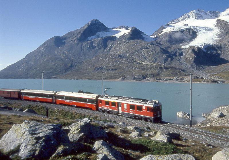 RhB REGIONALZUG von Tirano nach St.Moritz am 29.08.1993 an Nordende des Lago Bianco mit ABe 4/4III 54 - B 2491 - B 2461 - DZ. Hinweis: gerade Sonnenaufgang an dieser Fotostelle. Ich hatte Glck, da der Zug nicht 1 Minute vorher kam.
