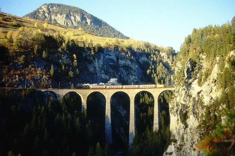 RhB Salondampfzug 3562 von Filisur nach Landquart am 26.10.1997 auf Landwasser-Viadukt zwischen Filisur und Alvaneu mit Dampflok G 4/5 107 - As 1144 - As 1142 - As 1141 - As 1143 - Xk 9044 - Hinweis: Der Salondampfzug fuhr in der 117-jhrigen Geschichte der RhB nur am 26.10.1997 mit einer Dampflok wenige Sekunden vor Sonnenuntergang ca. 16:08h Winterzeit noch bei ein wenig Streiflicht ber den Landwasser-Viadukt. Der hier ab Filisur am Zugschlu sichtbare, mitgefhrte Heizwagen X k 9045 war ntig, da die Salonwagen keine Dampfheizung haben und die 160 Franken zahlenden Fahrgste bei Auentemperaturen von wenig ber 0 nicht frieren sollten. - Hinweis: gescanntes Dia
