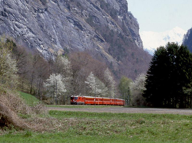RhB Schnellzug 44 von Davos-Platz nach Landquart vom 25.04.1992 mit E-Lok Ge 4/4II 614 - A - B - A - B - B - B - D. Hinweis: Der Schnellzug hat gerade das 1962/63 erbaute 983,60m lange Klus-Tunnel verlassen (Klusschlucht = Talenge zwischen Prttigau und Rheintal) und hat nur noch wenige Minuten Fahrzeit bis Landquart. Kurz nach der hohen Felswand und den blhenden Bumen weitet sich die Landschaft bei Malans. Das nchste Foto ist von gleichen Standpunkt, Sicht nur 90 links!