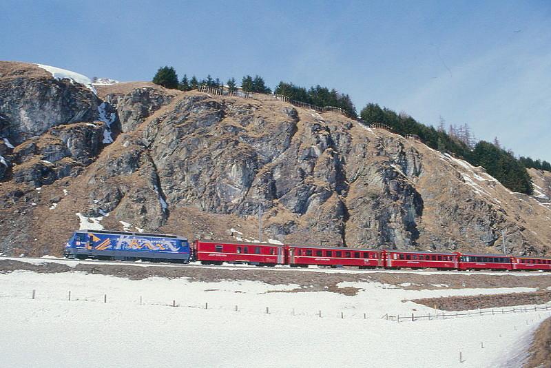 RhB Schnellzug 535 von Chur nach St.Moritz am 26.02.2000 zwischen Samedan und Celerina mit E-Lok Ge 4/4III 645 - D 4217 - B 2448 - B 2364 - B 2491 - A 1240 - A 1282 - A 1271 - B 2450 - B 2383 - B 2256. Hinweis: Lok-Werbung TV, gescanntes Dia
