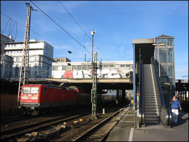 S-Bahn-Haltepunkt Dsseldorf-Wehrhahn am 15.12.2006. Sowohl der Haltepunkt selbst als auch das Umfeld machen keinen sehr ansprechenden Eindruck. Ein Regionalzug mit BR 112 166 an der Spitze passiert den Haltepunkt gerade in Richtung Dsseldorf Hbf.