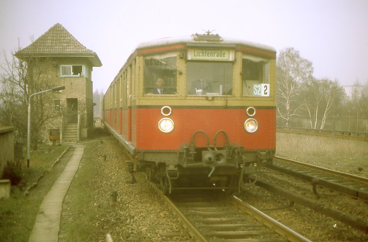 S - Bahn nach Lichtenrade beim Bahnhof  Priesterweg . Beachte das alte Stellwerk und die alte, etwas morsch wirkende Holzverkleidung der Stromschiene. April 1984