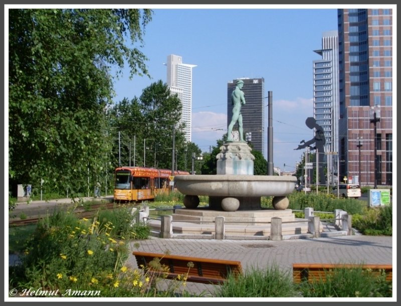 S-Triebwagen 230 als 2. Zug der Linie 17 zum Rebstockbad am 06.06.2008 kurz vor der Haltestelle Ludwig-Erhard-Anlage hinter dem Merkurbrunnen, einem neoklassizistischen Zierbrunnen aus dem Jahr 1916, entworfen von Hugo Lederer als Stiftung des Bankiers A. L. A. Hahn. Der Merkur weist auf das hinter dem Brunnen gelegene Messegel�nde hin. Am Bildrand halbrechts zwischen den Hochh�usern der  Hammering Man  ein Kunstwerk des US-amerikanischen K�nstlers Jonathan Borofsky. 