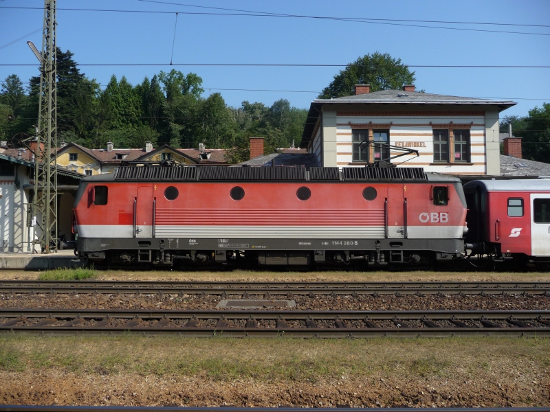 Seitenansicht der 1144 280-5, die gerade in der Bahnhaltestelle Rekawinkel mit einem CityShuttle-Zug hlt. (21.08.09)