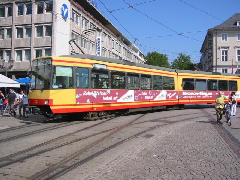 Stadtbahnwagen 587 (Typ GT8-80C) des KVV kommt am 04.09.2004 aus Richtung des Karlsruher Hauptbahnhofs und biegt beim Gleisdreieck am Marktplatz in die Fugngerzone Kaiserstrae ein. Das Fahrzeug fhrt auf der Linie S1 und hat den Karlsruher Stadtteil Neureut zum Ziel. Da die Haupt-Fugngerzone von Karlsruhe durch die vielen S- und Straenbahnen ziemlich verstopft wird, ist ein Tunnel unter der Kaiserstrae in der Planung, der all die Bahnen aufnehmen soll, so dass die Fugngerzone irgendwann ausschlielich den Fugngern gehren soll (U-Strab-Projekt). Das Bild macht deutlich, dass das Nebeneinander von groen Stadtbahnwagen und Leuten innerhalb einer Fugngerzone nicht ganz unproblematisch ist. Den Fahrern dieser Bahnen ein groes Kompliment fr ihr zumeist sehr umsichtiges Fahrverhalten; Unflle mit Fugngern sind hier sehr, sehr selten.