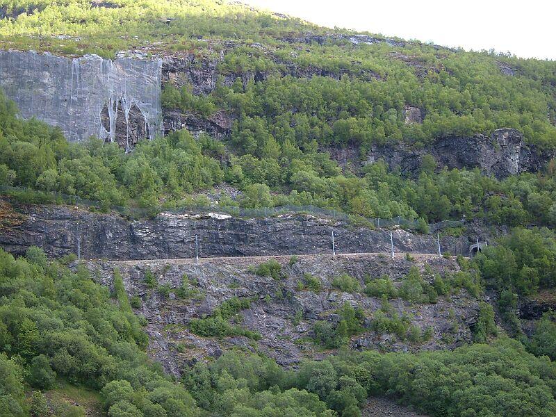Streckenabschnitt zwischen dem Blomheller-Tunnel 1030 m lang und dem Nali-Tunnel 1342 m lang, etwas weiter links liegt die Bedarfshaltestelle Kardal, 556 m hoch, km 13,9 von Flam. Beachtliche Gre hat das Steinschlag-Schutznetz, aber auch ein paar Lcher. Leider kam ein Zug ein paar Minuten zu frh, da verdeckten Bume die Sicht.