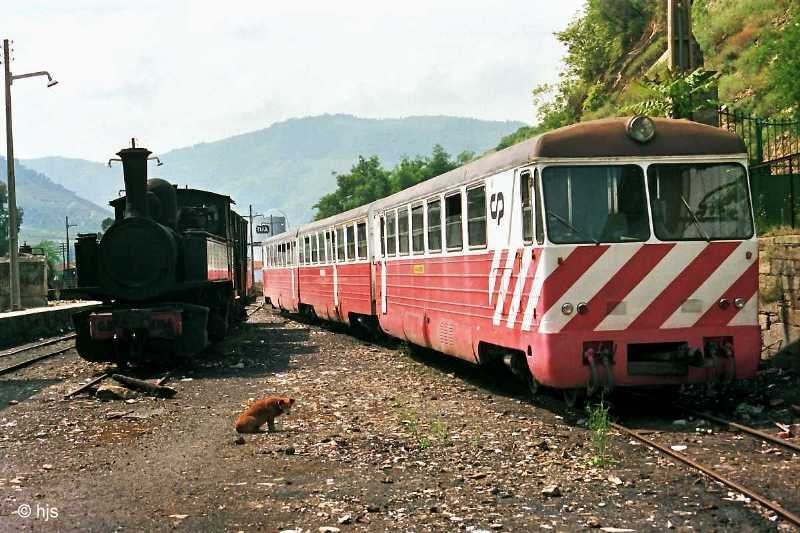 Szene mit Hund. Auf dem Bahnhofsgelnde von Tua steht rechts der Triebzug 9702/9732/9701, links rostet Lok E 164 einer ungewissen Zukunft entgegen, dazwischen der Bahnhofshund (12. Mai 1988). - In Tua nimmt die  Linha do Tua  nach Bragana ihren Ausgang, die jedoch seit 1990 nur noch bis Mirandela befahren wird.