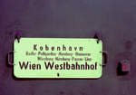 DSB: Schild:  København - Rødby - Puttgarden - Hamburg - Hannover - Würzburg - Nürnberg - Passau - Linz - Wien Westbahnhof . - Einmal gab es vom Kopenhagener Hauptbahnhof mehr Kurswagen als heute ins große Ausland, u.a. nach Wien (Westbahnhof), einer Stadt, zu der ich mehrmals mit der Bahn gefahren bin. -  Wegen der kritischen Gesundheitslage (Corona) und der aus diesem Grund auferlegten Restriktionen reisen die meisten viel weniger als früher, aber hoffentlich wird es im Laufe des neuen Jahres wieder möglich sein, die Staatsgrenzen ohne Probleme mit der Bahn (oder auf eine andere Weise) zu passieren. - Ort: København H (: Kopenhagen Hauptbahnhof). Zeit: August 1975. - Scan eines Farbnegativs. Film: Kodak Kodacolor II. Kamera: Kodak Retina Automatic II.  