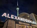 Abendliche Momentaufnahme am Bahnhof Alexanderplatz mit dem Fernsehturm, der Bahnhofshalle und dem passenden Schriftzug.