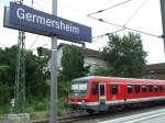 Das Bahnhofsschild von Germersheim mit einem VT 628 im Hintergrund.