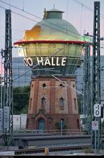 Durchblick auf den beleuchteten Wasserturm mit Werbung für den Bergzoo Halle am Abend in Halle(Saale)Hbf.