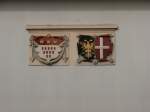 Die Wappen der Städte Köln und Neuss hängen stolz an einer Wand eines Gebäudes im Neusser HBF.
