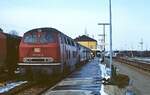 In Aulendorf wartet die 215 130-6 mit zwei Umbau-Vierachsern am 12.02.1983 auf die Abfahrt. Wie man zwischen Lok und erstem Wagen erkennen kann, arbeitet die Dampfheizung an diesem kalten Wintertag.