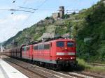 151 020-5 mit Schwesterlok ziehen einen langen Gterzug durch Kaub, das von der Burg Gutenfels berragt wird.