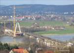 Whrend eine  Kndelpresse  (BR 180) in Farbgebung DR auf der Brcke die Elbe berquert, schiebt sich ein Frachtkahn an der Baustelle fr die neue Straenbrcke vorbei - Niederwartha, 09.03.2007  