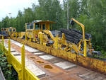 Blick über einen Flachwagen mit Rungen auf das in Hattinger Bahnhofsnähe abgestellte schwere Bahnbaugerät, wie zum Beispiel die Schotterplaniermaschine SSP 110 SW.