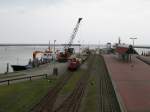 26.07.2007: K 1 der Inselbahn Langeoog vor einem Gterzug im Hafenbahnhof der Insel whrend der Beladung, links am Anleger das Gterschiff aus Bensersiel
