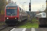Ein Dostosteuerwagen der 3. Generation fährt am 3.11.2025 als RB51 nach Wächtersbach in Hailer-Meerholz ein. Im Linken Scheinwerfer kann man noch den vorangegangenen Fernlichtgruß erkennen. Im Hintergrund kann man ebenso noch einen ICE 4 auf seiner Fahrt nach Frankfurt und weiter in die große weite Welt sehen.
