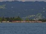 Blick von Lindau-Bad Schachen auf das Badehaus von Lindau-Aeschach und den Bodenseebahndamm, auf dem gerade IRE 4214 auf der Fahrt nach Ulm den Startbahnhof Lindau verlassen hat (17.08.2013).