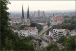 Ein Städtefoto mit Stadtbahn -    Blick vom Hang des Johannisberges auf Bielefeld mit den spitzigen Türmen der Neustädter Marienkirche und dem Landgericht rechts.