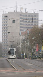 Wagen 305 der Dessauer Verkehrsgesellschaft (DVG) ist auf dem letzten Teilsück (durch die Fritz-Hesse-Straße) der Linie 1 kurz vor dem Ziel Hauptbahnhof unterwegs. Rechts im Bild die Haltestelle  Theater  und im Hintergrund eines der markaten  Y-Häuser  der Stadt, in dem Fall die grüne Variante.

Dessau, der 05.02.2021