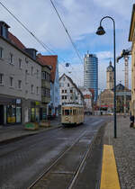 Am 29.11.2025 war Tw 26 der Jenaer Straßenbahn auf einer Sonderfahrt unterwegs. Gerade ist er in den Steinweg eingebogen und zeigt sich vor der Kulisse des Jentowers und der St. Michaels-Kirche.