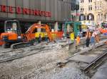 In den Sommerferien 2005 wurden wieder Straenbahngleise in der Karlsruher Innenstadt gewechselt, hier am Europaplatz. Die Folge waren wieder umfangreiche Umleitungen. Die Aufnahme stammt vom 23.08.2005. Die alten Gleise sind entfernt worden, jetzt beginnt die Bearbeitung des Untergrunds. Die im Bild sichtbaren Weichenteile blieben liegen; das Gleisdreiecke am Europaplatz war schon vor einiger Zeit erneuert worden.